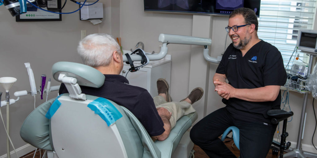 dr alptekin discussing dental procedure process to older man in dental chair